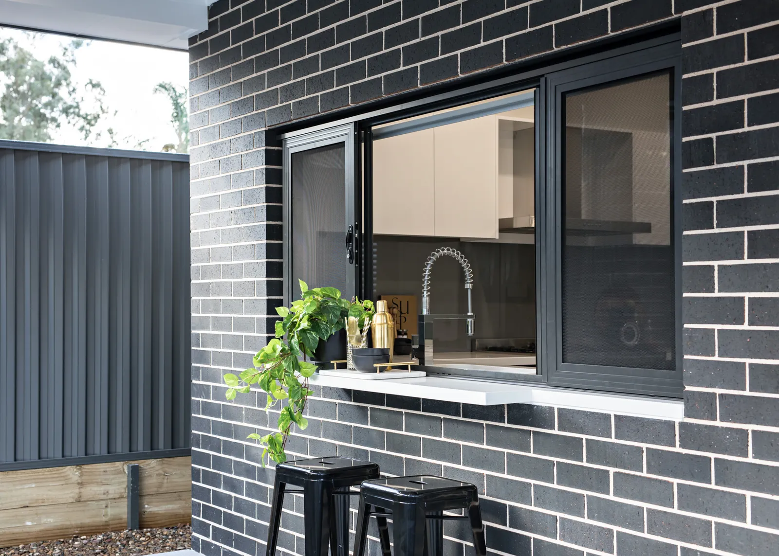 Custom home outdoor servery window with dark brick and black frames